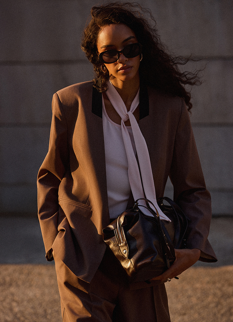 Промотира елегантен дамски тоалет, съчетаващ втален костюм с блуза и чанта, подходящ за професионална среда и изискано ежедневно носене.