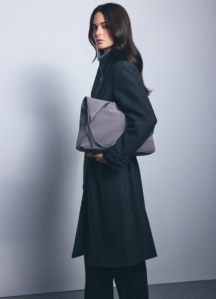 Žena u dugom elegantnom kaputu drži veliku torbu za rame, predstavljajući minimalistički smart-casual modni stil