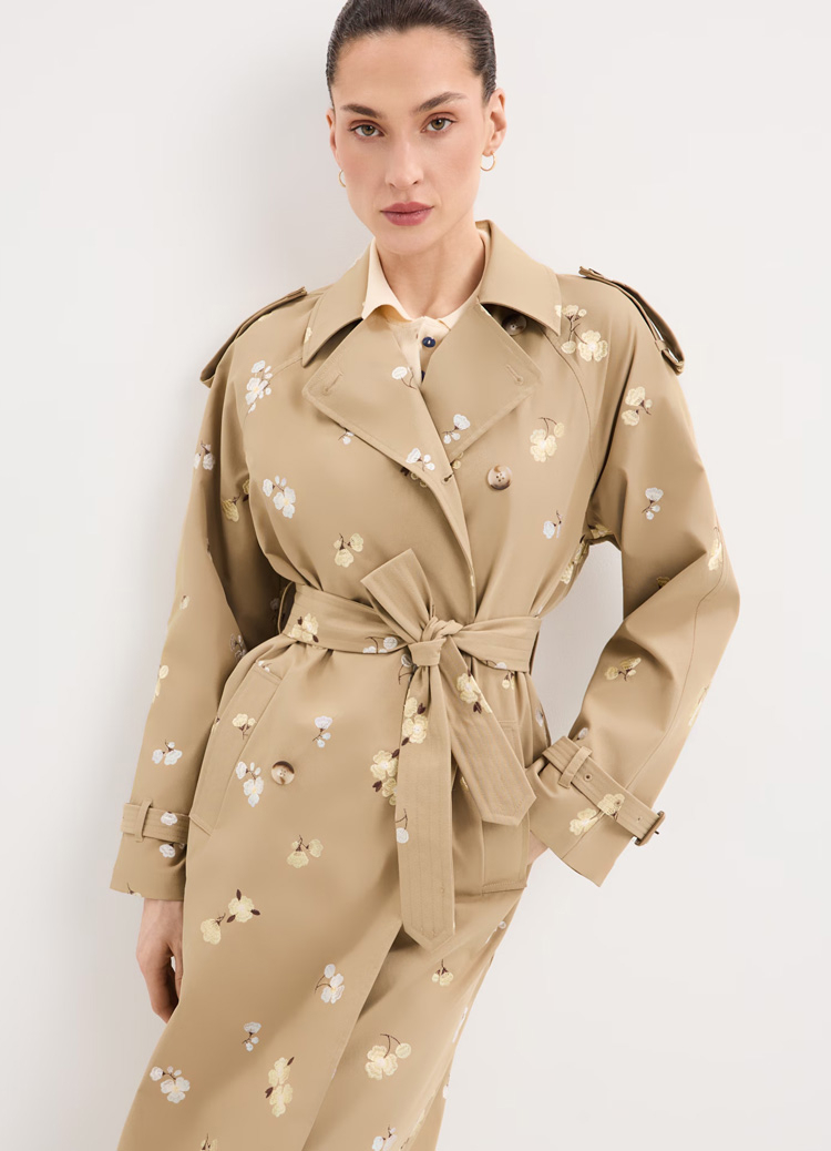 Ženski trenč mantil sa pojasom i cvetnim printom, prikazan na modelu radi predstavljanja kroja, siluete i ukupnog stila u online modnoj ponudi.