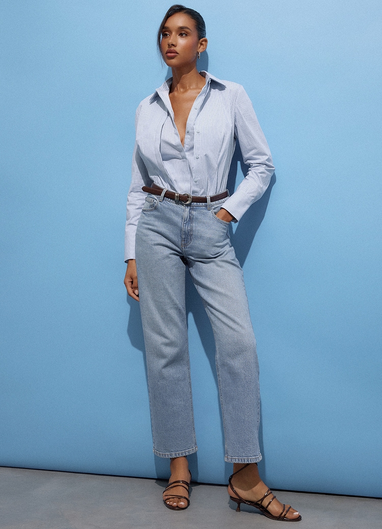 Žena nosi prugastu usku košulju, farmerke ravnog kroja, kaiš i sandale sa štiklom u prezentaciji smart casual stila