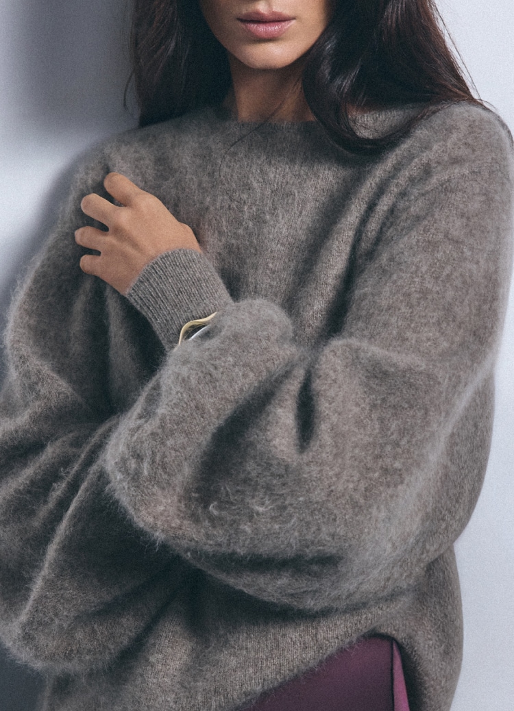 Žena nosi mekani oversized pleteni džemper opuštenog kroja, naglašavajući udoban svakodnevni modni stil