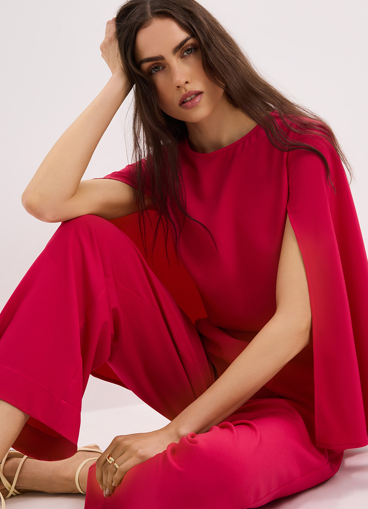 Elegantna ženska kombinacija sa gornjim delom u stilu pelerine i pantalonama širokih nogavica, predstavljena radi prikaza kroja i stila za formalne ili svečane prilike.