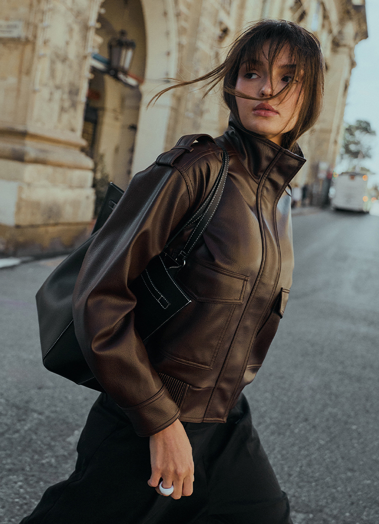 Miejski obraz stylu życia przedstawiający osobę idącą przez miasto w kurtce i z plecakiem, ukazujący codzienne zastosowanie mody oraz praktyczność w ruchu.