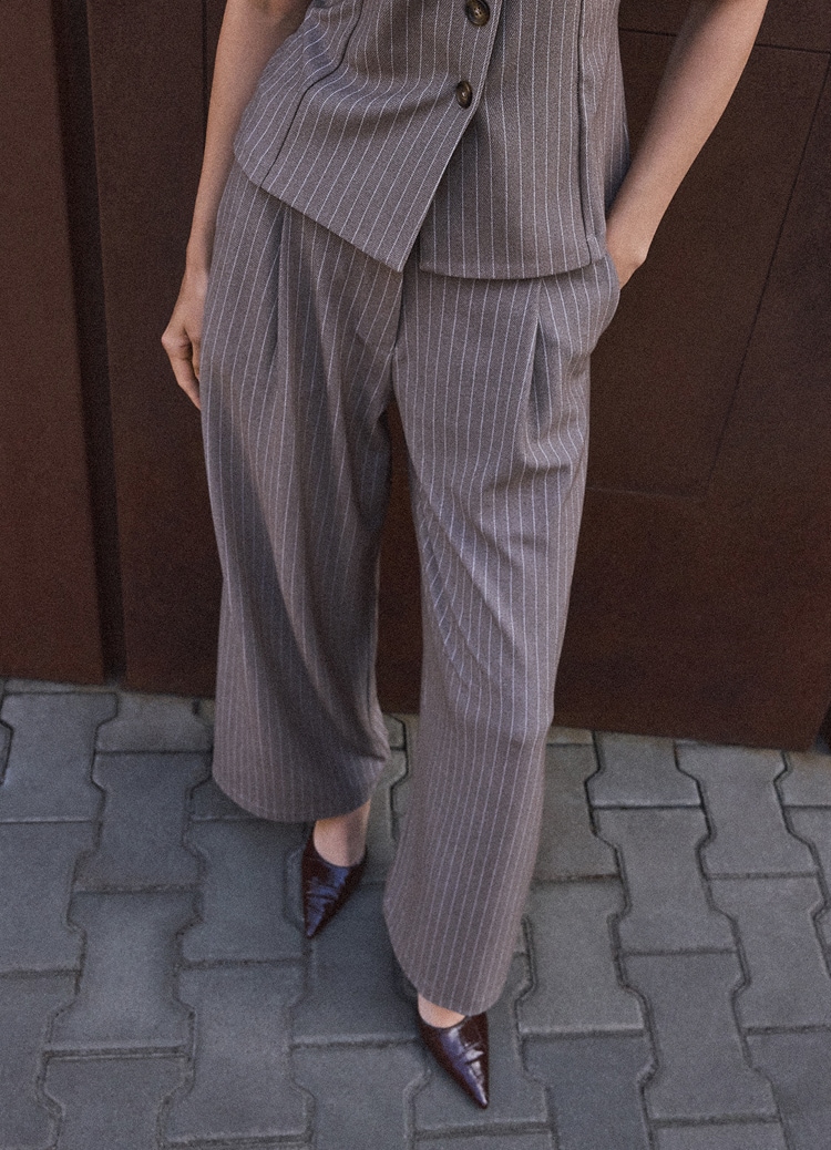 Femeie purtând pantaloni eleganți cu dungi și croială largă, asortați cu o vestă și pantofi cu vârf ascuțit pentru o ținută smart casual