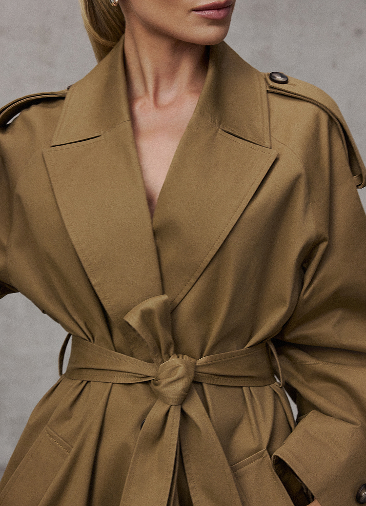 Zdjęcie produktu przedstawiające trencz z paskiem, podkreślające dopasowany krój, szeroki kołnierz oraz regulowane wiązanie w talii, aby oddać elegancki i wszechstronny styl odzieży wierzchniej.