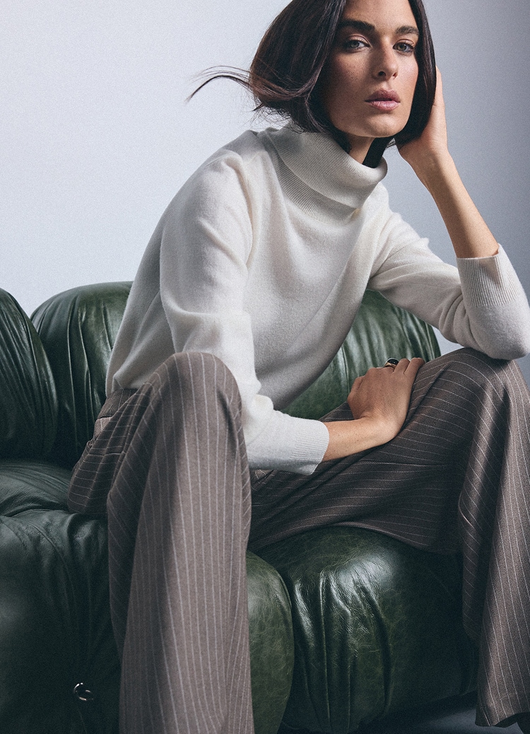 Жена с поло и раирани панталони в елегантен smart casual стил, седнала в кресло